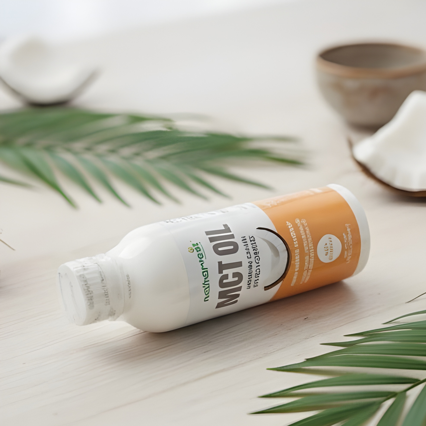 Bottle of MCT oil on a light wooden surface with green leaves